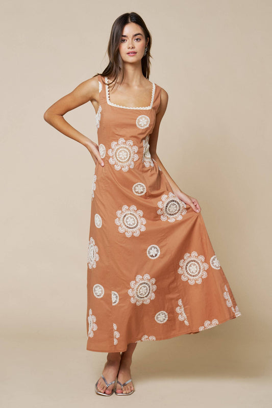 Woman wearing a caramel brown dress with white floral patterns on a beige background