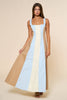 Woman wearing a long, color-blocked dress with beige, blue, and yellow sections on a beige background.