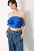 Woman wearing a blue ruffled top and denim pants against a plain background
