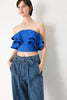 Woman wearing a blue ruffled top and denim pants against a white background