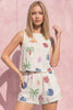 Woman wearing a sleeveless top and shorts with colorful palm tree and flower patterns against a pink background