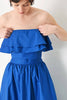 Woman wearing a blue strapless dress against a plain background