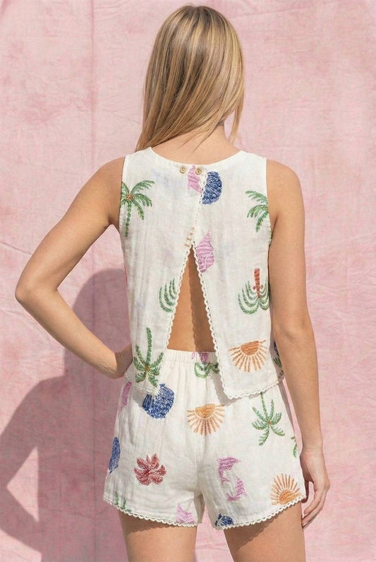 Woman wearing a white embroidered romper with colorful designs against a pink background