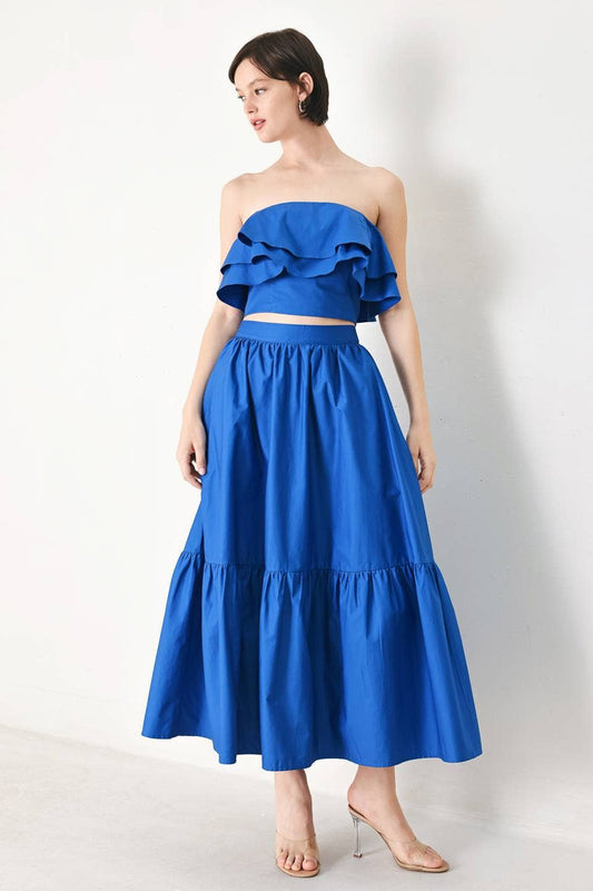 Woman wearing a blue two-piece outfit with a ruffled top and tiered skirt on a white background